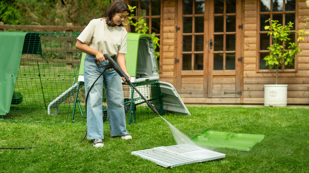 woman pressure washing the pull out parts of the eglu go up chicken coop