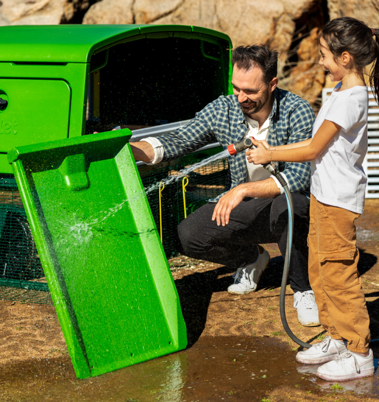 father and daughter cleaning the eglu pro with a hose pipe
