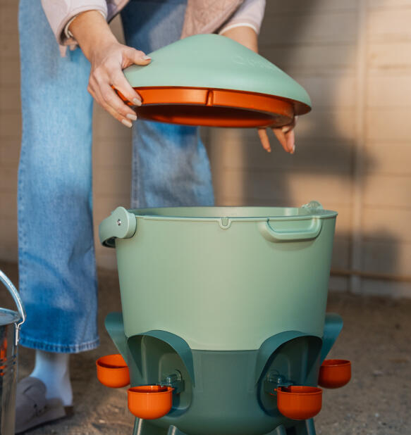 woman lifting the locking lid on the omlet insulated chicken waterer